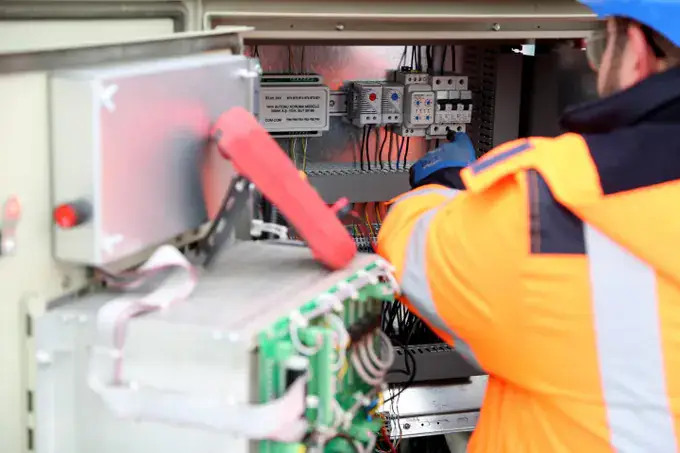 Technician in a hard hat and high-visibility jacket working in an equipment cabinet