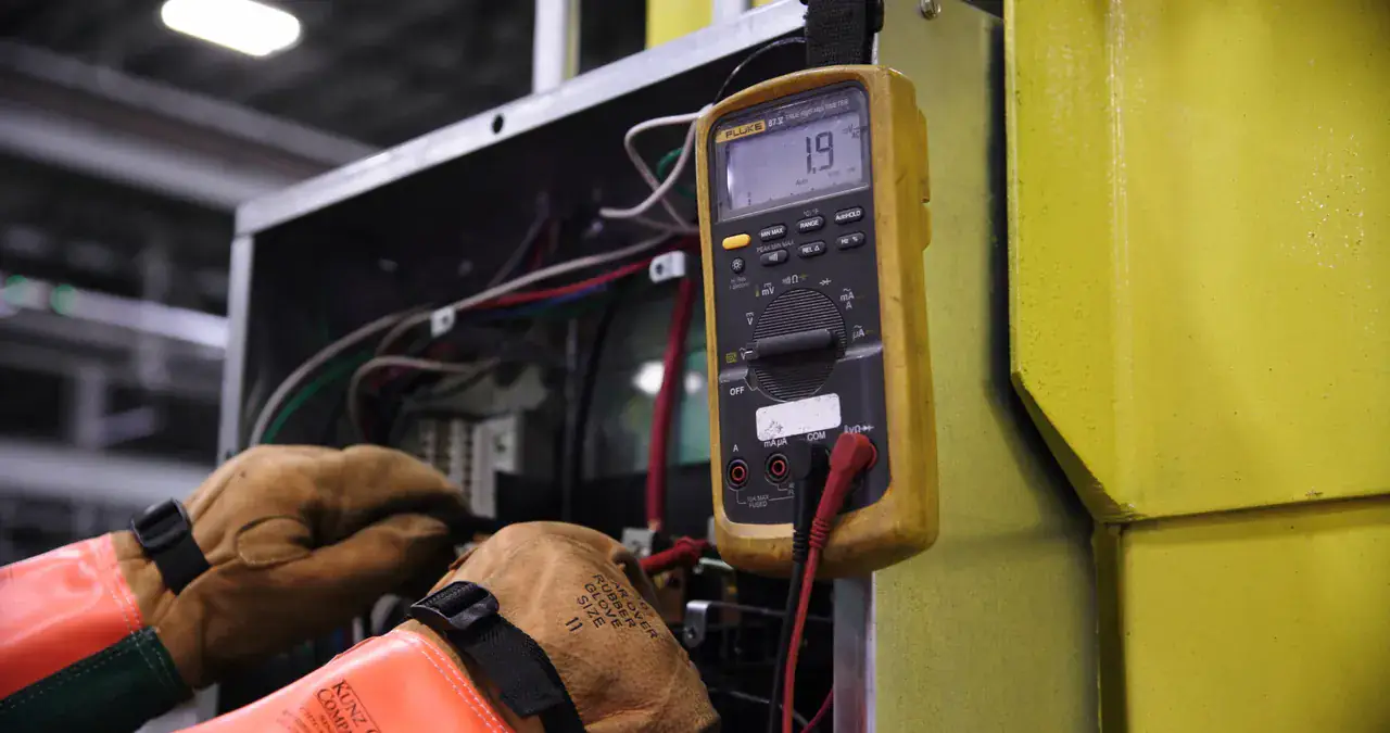Gloved hand holding a multimeter inside an equipment cabinet