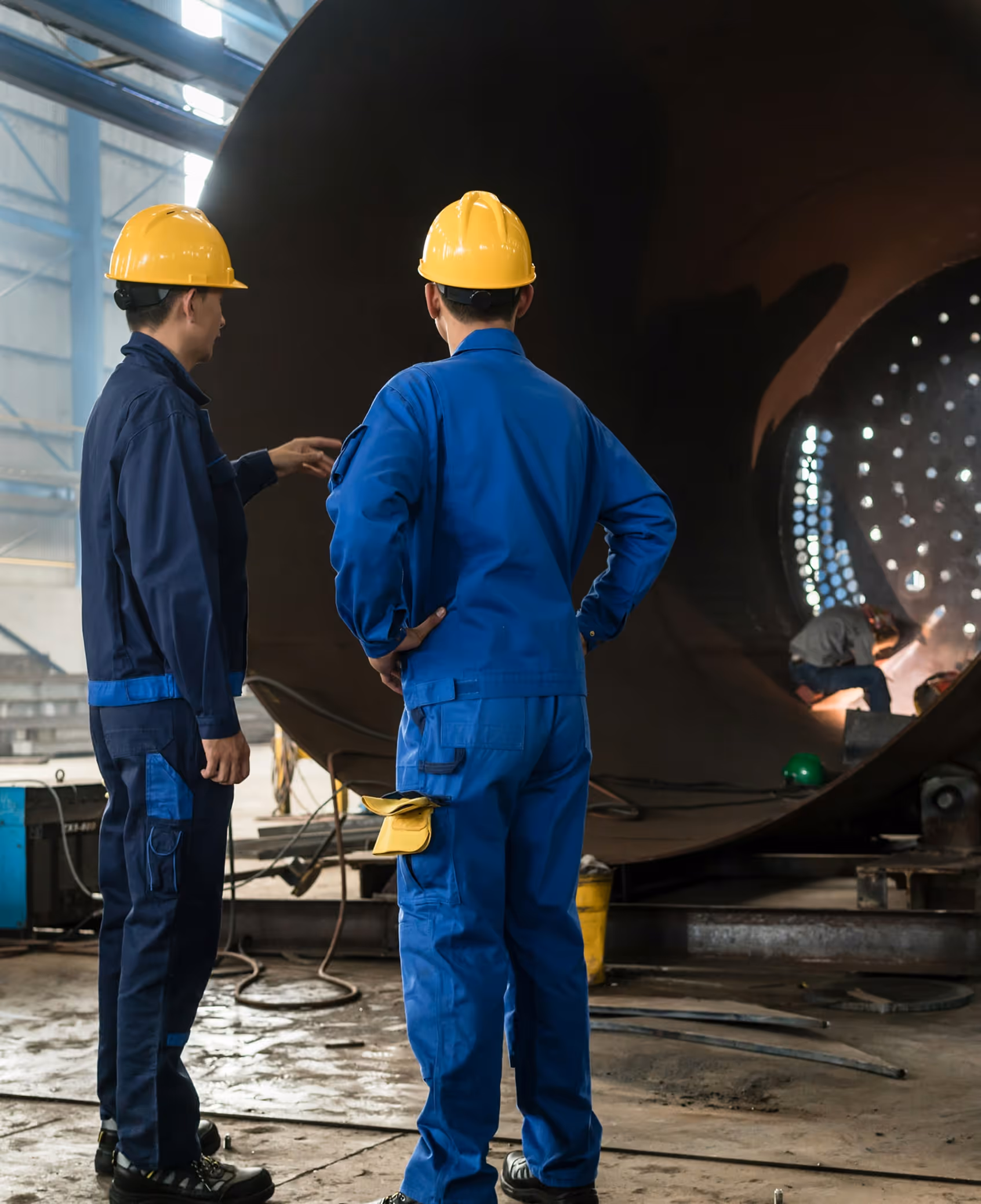Two workers in hard hats and coveralls inspecting large industrial equipment