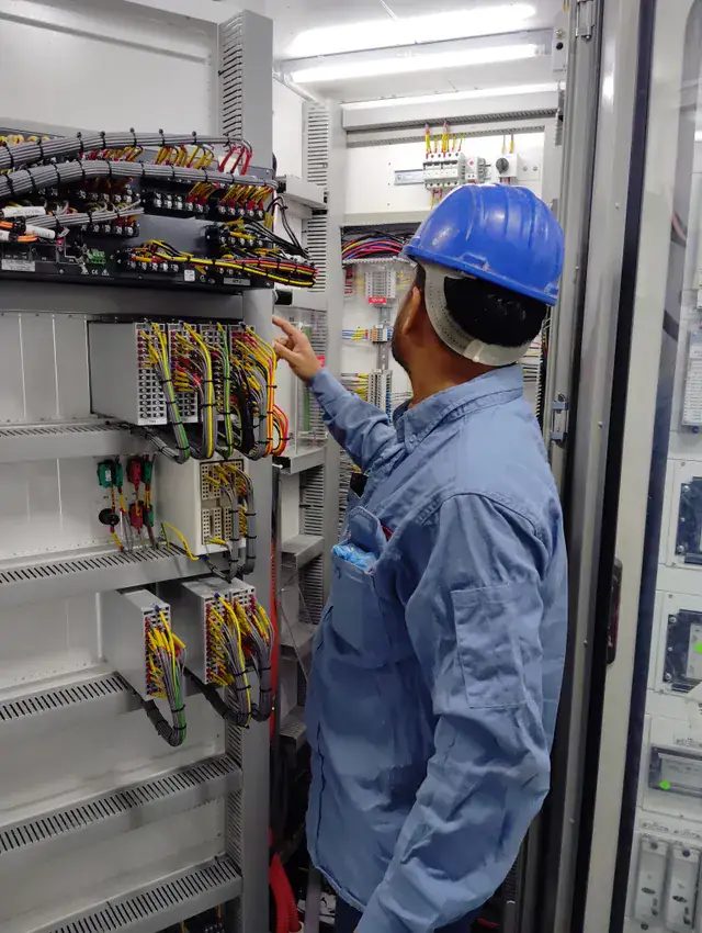 Electrician in a blue hard hat checking wiring in a tall control cabinet