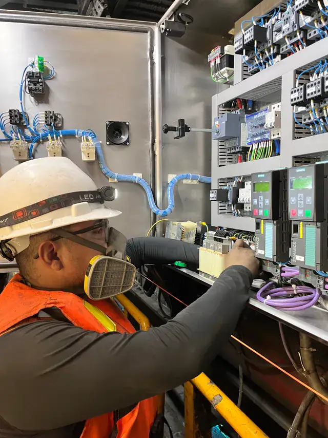 Technician in a hard hat and respirator working on industrial drive controls