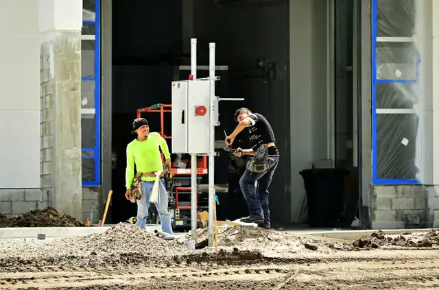 Two workers beside a temporary electrical panel on an open construction site
